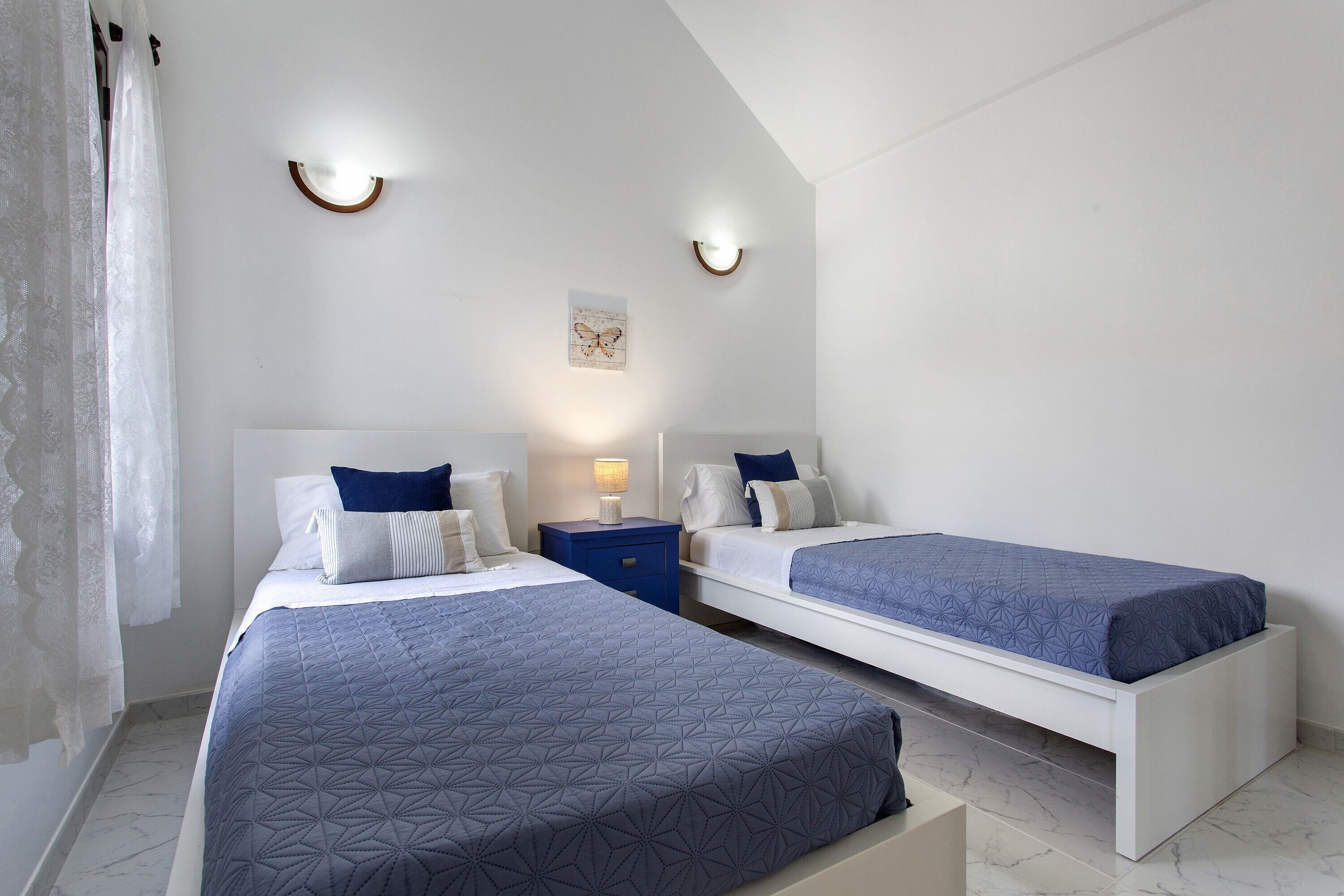 Une chambre avec deux lits, une table de chevet, une lampe fixée au mur et une petite œuvre d’art.