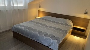 A modern bedroom with a wooden bed frame, a patterned bedspread, and built-in nightstands with wall-mounted lamps. - Apartment in Punat with Seaview, Terrace, Air condition, WIFI (4534-2) (Punat)