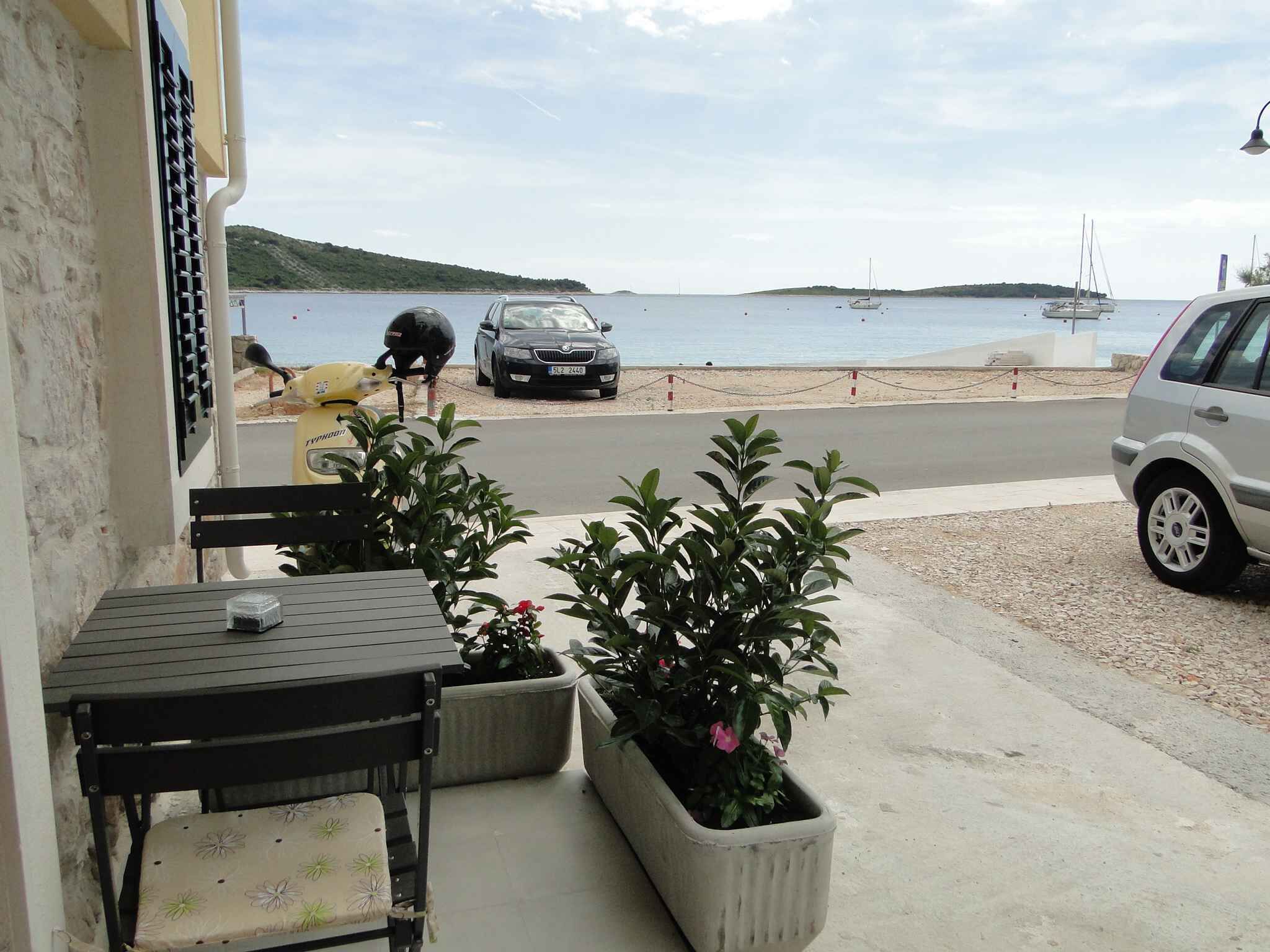 A seaside view with a road leading to the beach, a parked car, and a table with chairs on the porch.