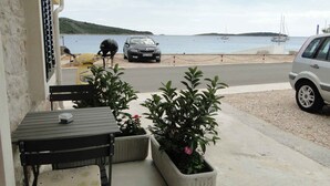 A seaside view with a road leading to the beach, a parked car, and a table with chairs on the porch. - Studio with terrace and sea view (Primošten)