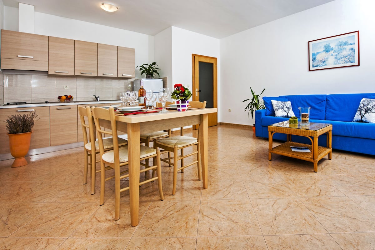 Une cuisine moderne avec des meubles en bois, une table à manger avec des chaises, un canapé bleu et une table basse en osier.