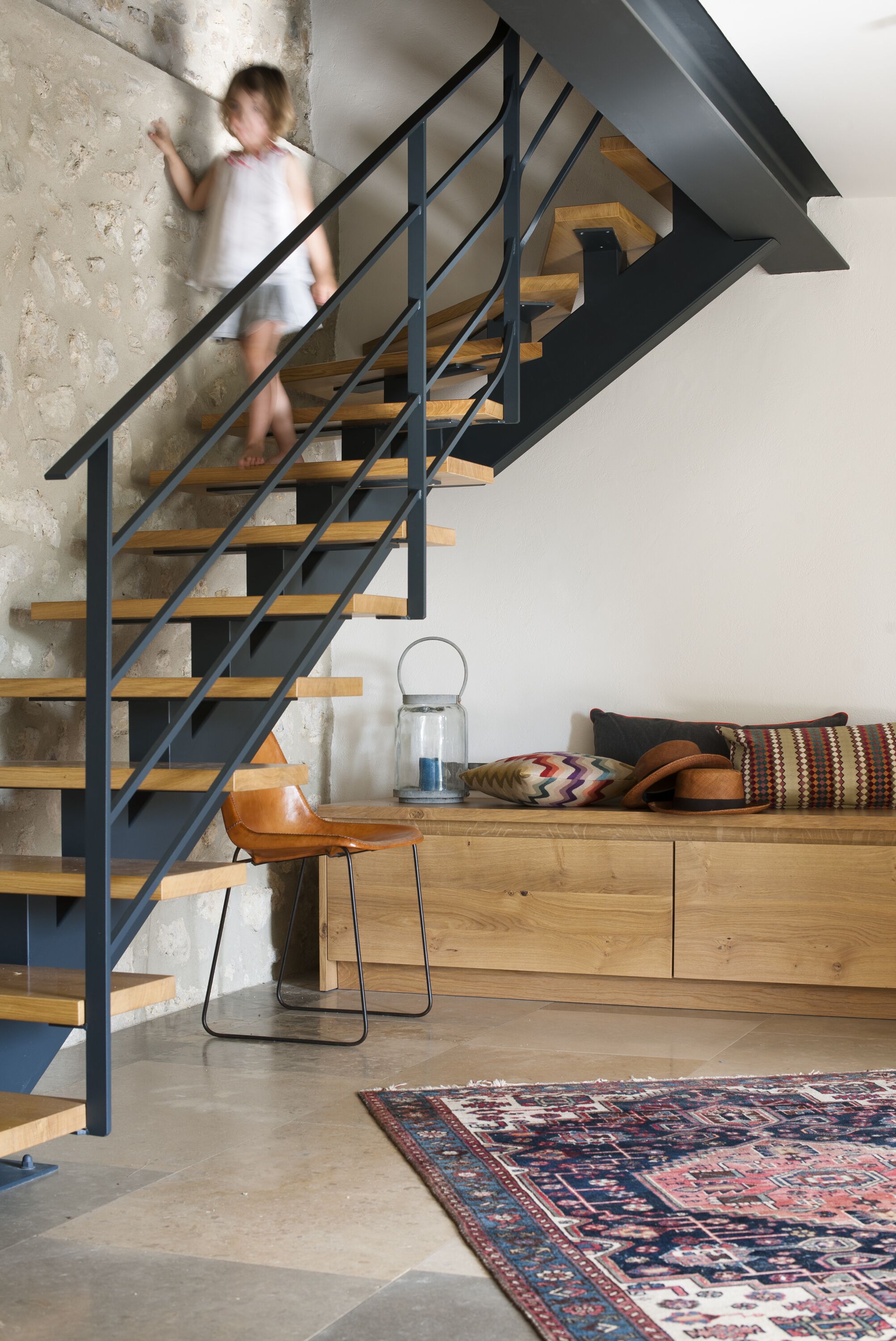 A staircase with a wooden finish and black metal railings, leading to a wooden bench area with cushions and a glass lantern.