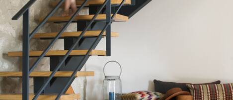 A staircase with a wooden finish and black metal railings, leading to a wooden bench area with cushions and a glass lantern.