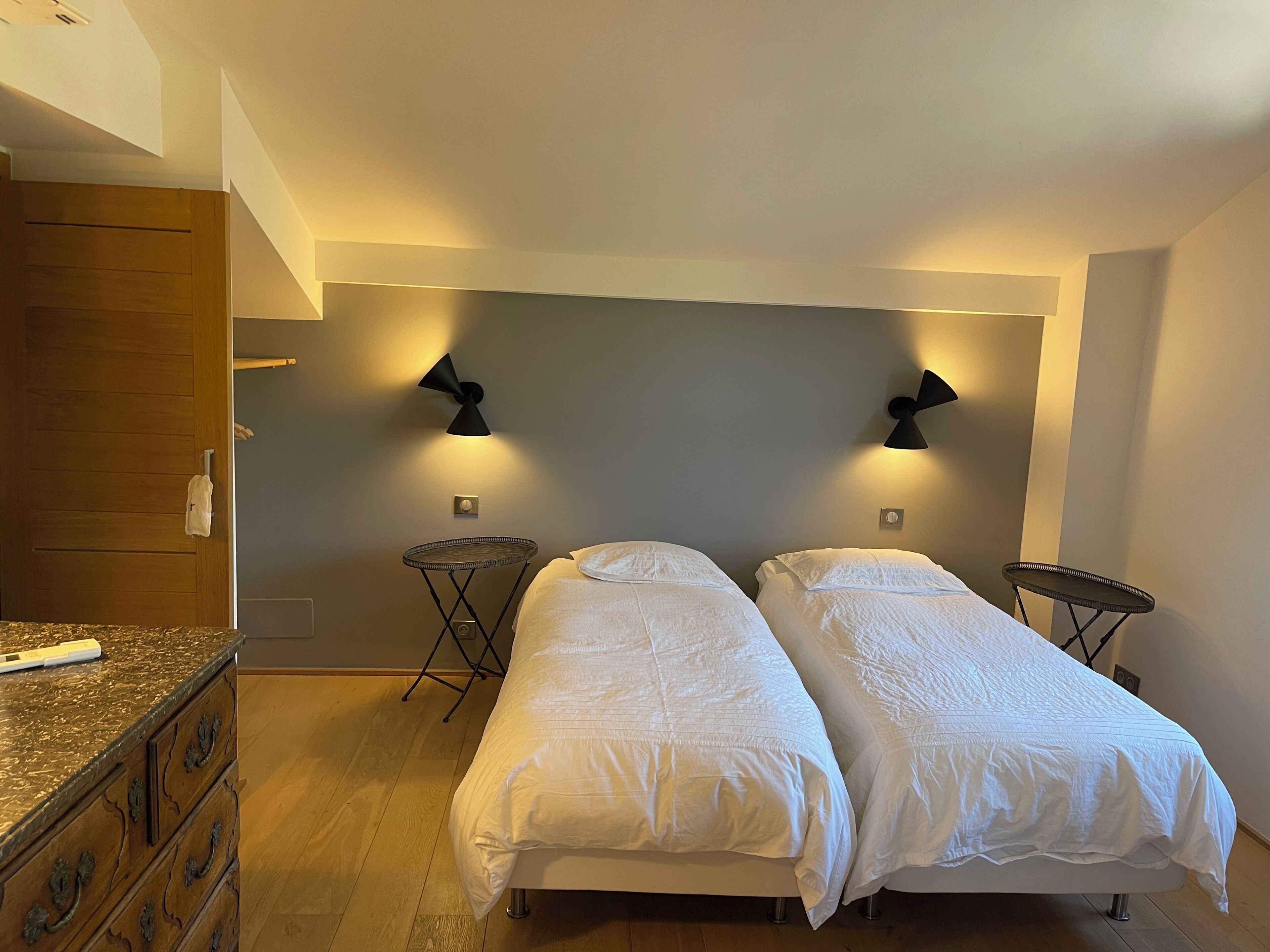 Una habitación con dos camas, un aparador de madera y dos lámparas fijadas a la pared.