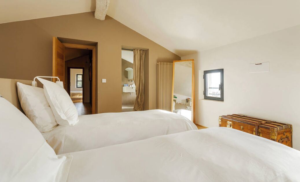 A hotel room with two beds, a wooden headboard, a mirror, a wardrobe, and a door leading to another room.