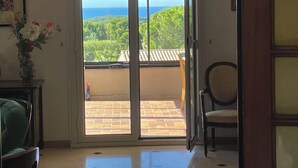 Ein Zimmer mit einer Schiebetür, die auf einen Balkon mit Blick auf Grünflächen und das Meer führt.