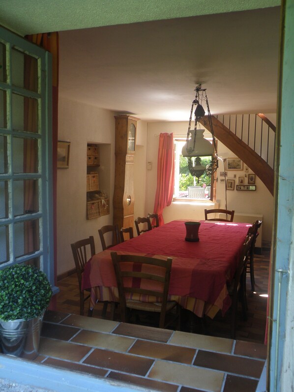 Un coin repas avec une nappe rouge, des chaises en bois, un luminaire suspendu et une vue sur l’extérieur par une fenêtre.