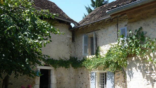Un edificio rustico in pietra con tetto in tegole, pareti ricoperte d'edera e un piccolo giardino con fiori e piante.