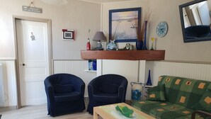 A living room with two dark blue armchairs, a green sofa, a wooden coffee table, and a painting above the sofa. - Charming renovated house, near beach and shops (La Faute-sur-Mer)