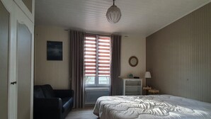 A bedroom with a bed, a nightstand, a lamp, a chair, a window with curtains, and a door. - Charming renovated house, near beach and shops (La Faute-sur-Mer)