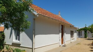 A white building with a tiled roof, a door, and a window. There are potted plants and a concrete path. - Charming renovated house, near beach and shops (La Faute-sur-Mer)