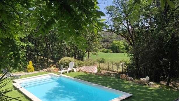 Piscina rodeada por vegetação exuberante e uma área cercada.