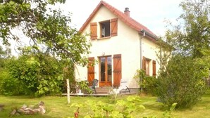 Een tweelaags huis met een rode pannendak, houten luiken en een veranda met buitenmeubilair.