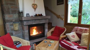 Een gezellige woonkamer met een stenen openhaard, rieten meubels en uitzicht op groen.