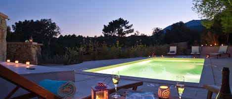 A poolside setting with a table, chairs, and a bottle of wine.