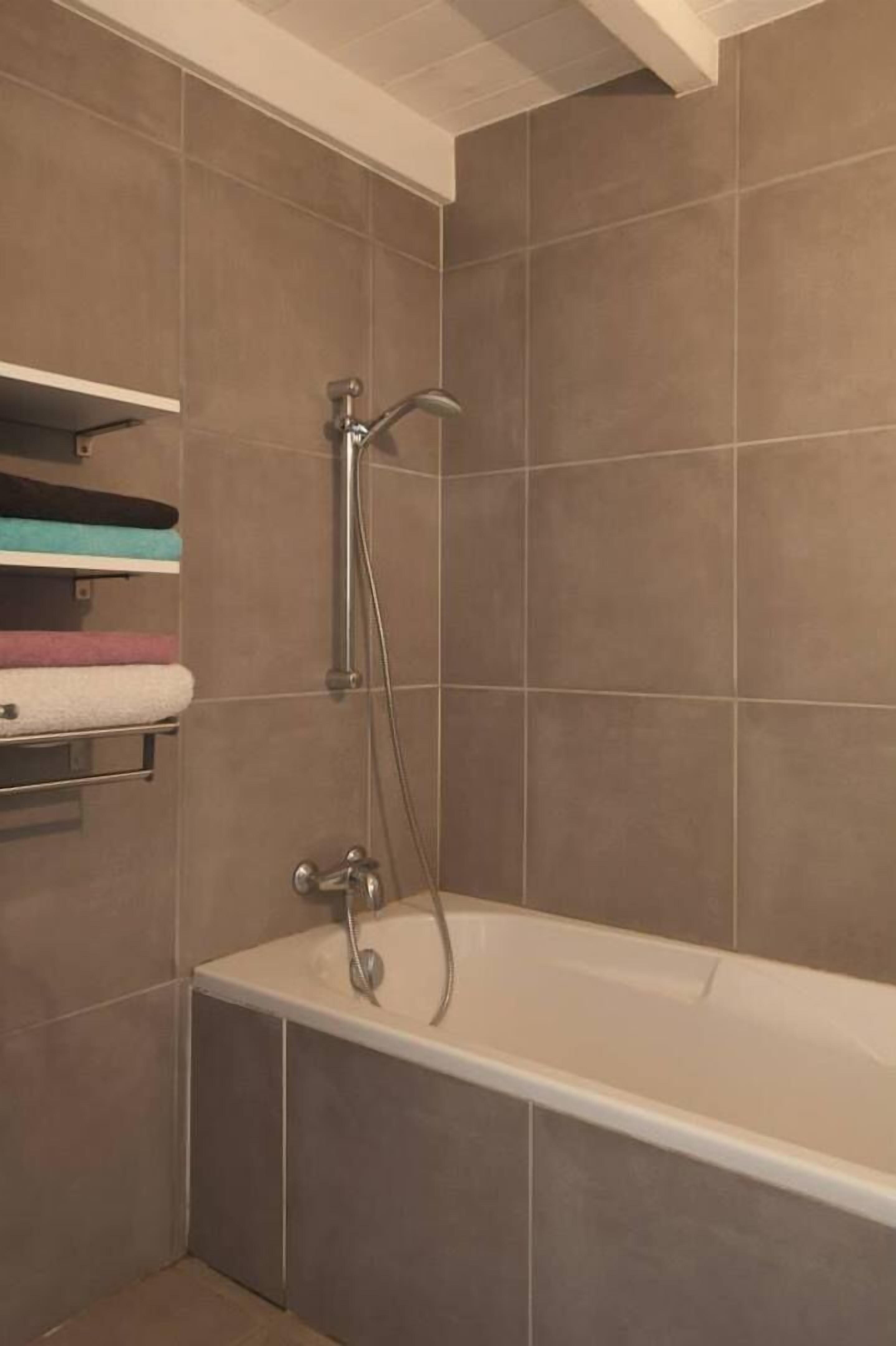 Een badkamer met een bad, douchekop en een handdoekrek met handdoeken.