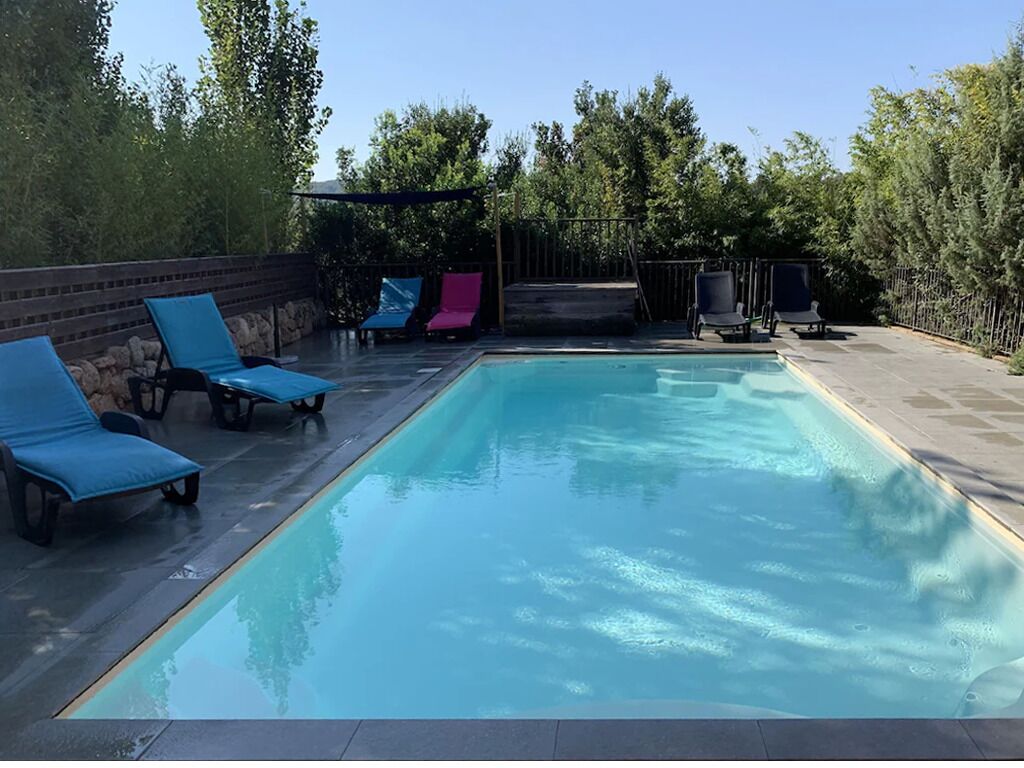 A rectangular swimming pool with blue and pink lounge chairs around it.