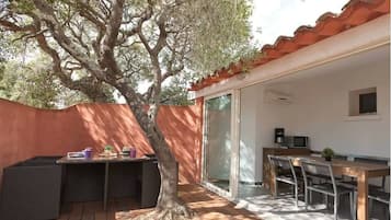 Eine Terrasse mit Esstisch und Stühlen, ein kleiner Tisch mit Gegenständen sowie ein großer Baum.