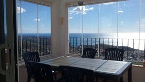 Un balcon avec une table et des chaises, offrant une vue sur la mer et les collines lointaines.