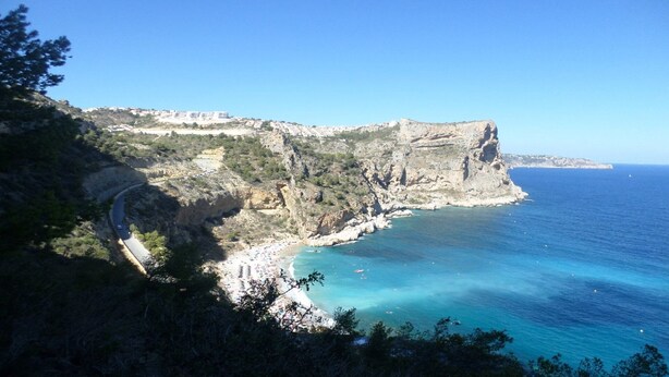 Un paysage côtier avec une falaise rocheuse, une route sinueuse et une mer bleue et limpide.