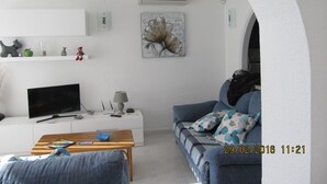Un salon moderne avec un téléviseur à écran plat, une table basse, un canapé et un tableau accroché au mur.