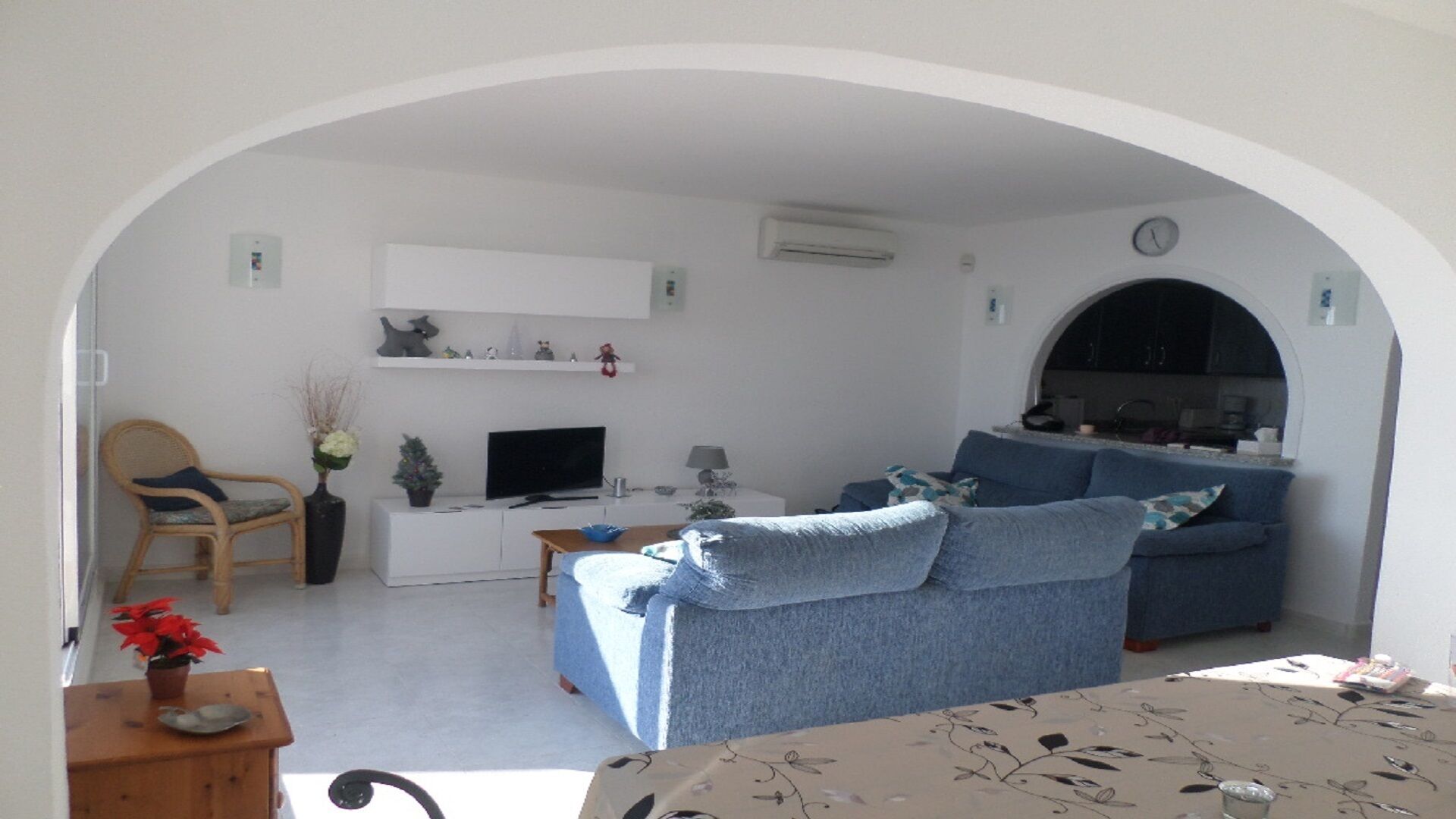 A living room with a sofa, a television, a small table with a vase, and a chair.