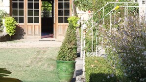 Un pati amb una porta de fusta, una paret de pedra i un jardí petit amb un arbre i plantes en testos.