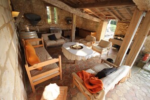 A rustic stone-walled room with a stone floor, wooden furniture, a round table, and a stone fireplace.