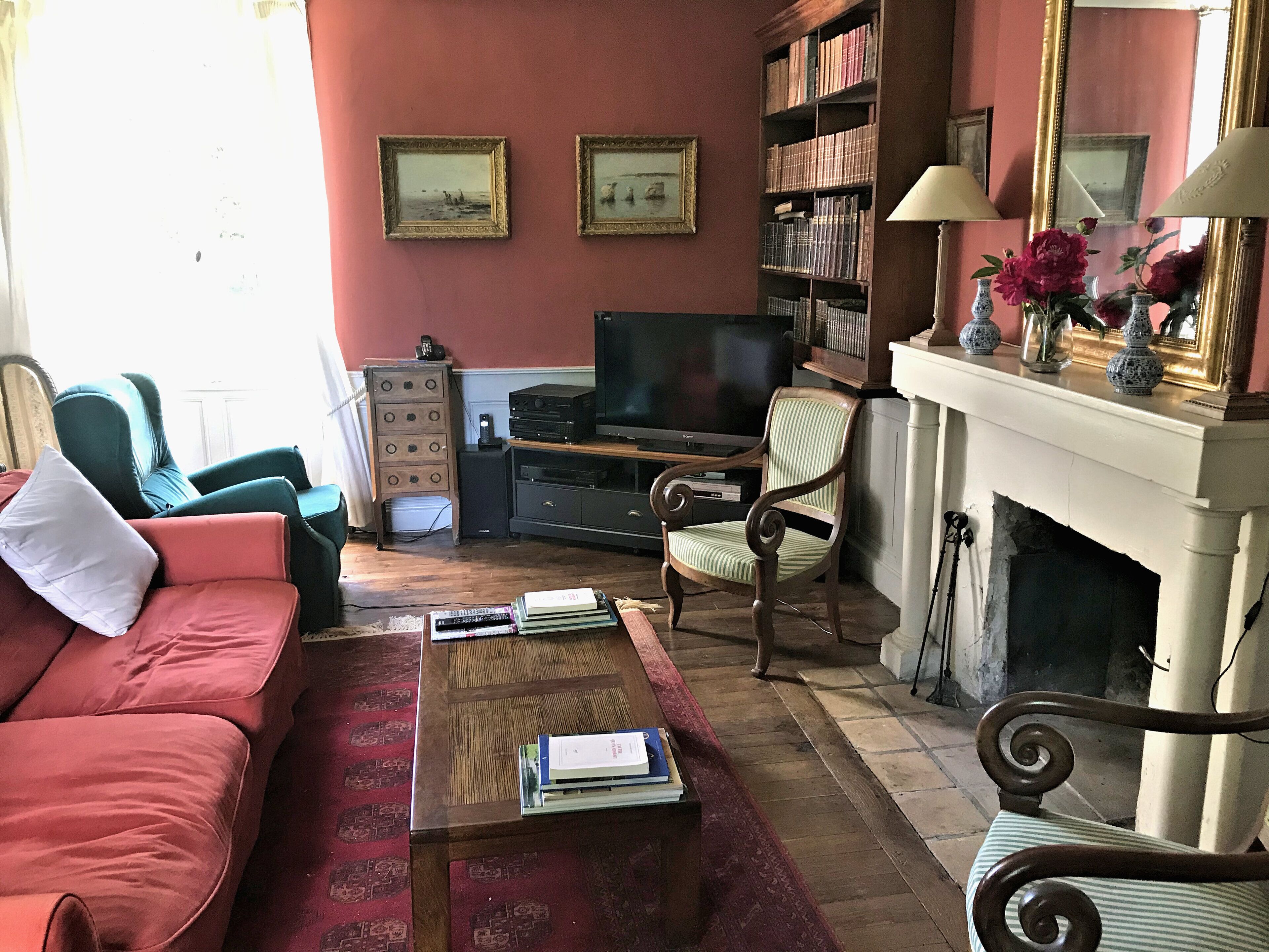 Un salon comprenant un canapé, des fauteuils, une table basse avec des livres, une cheminée et une bibliothèque.