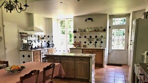 Una cocina con suelo de baldosas, una mesa de comedor con sillas, un refrigerador y una ventana con rejas decorativas.