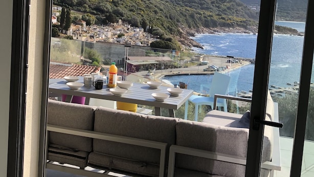 Un balcon avec vue sur une ville côtière, une piscine et une chaîne de montagnes en arrière-plan.
