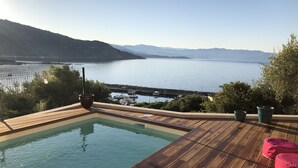 Une terrasse en bois avec une petite piscine, offrant une vue sur un plan d’eau paisible et des montagnes lointaines.