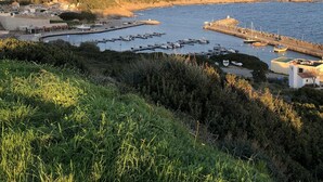 Un port de plaisance situé sur la côte, où sont amarrés des bateaux, et qui est entouré de collines et de bâtiments.
