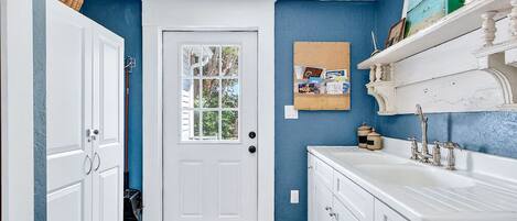 A bathroom with white cabinetry, a blue accent wall, a wooden floor, and a white door.
