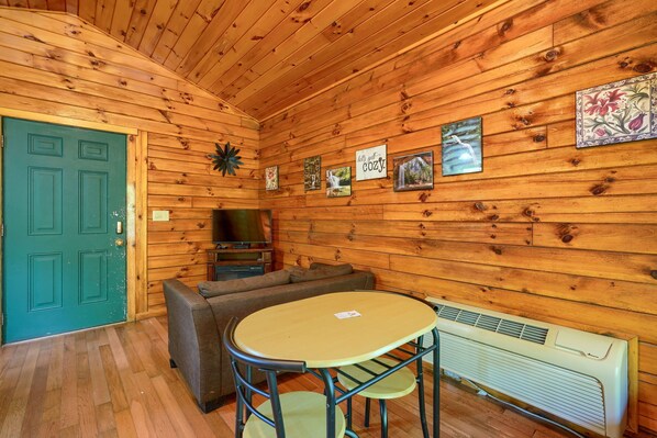 Interior acogedor de una cabaña con una puerta verde, un sofá, un televisor y una mesa con sillas.