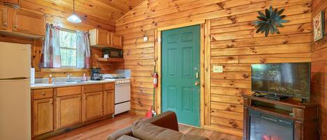 Interior acogedor de una cabaña con paredes de madera, una kitchenette, una puerta verde y una chimenea.