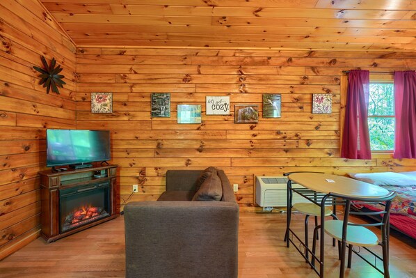 A cozy cabin interior with a fireplace, a television, a dining table, and a comfortable seating area.