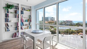 A modern room with a large window, white walls, and a bookshelf filled with books. - 🌅 Cozy Gulf-View Condo | Snowbird Rates & Sauna | Shoreline 3063 (Destin)