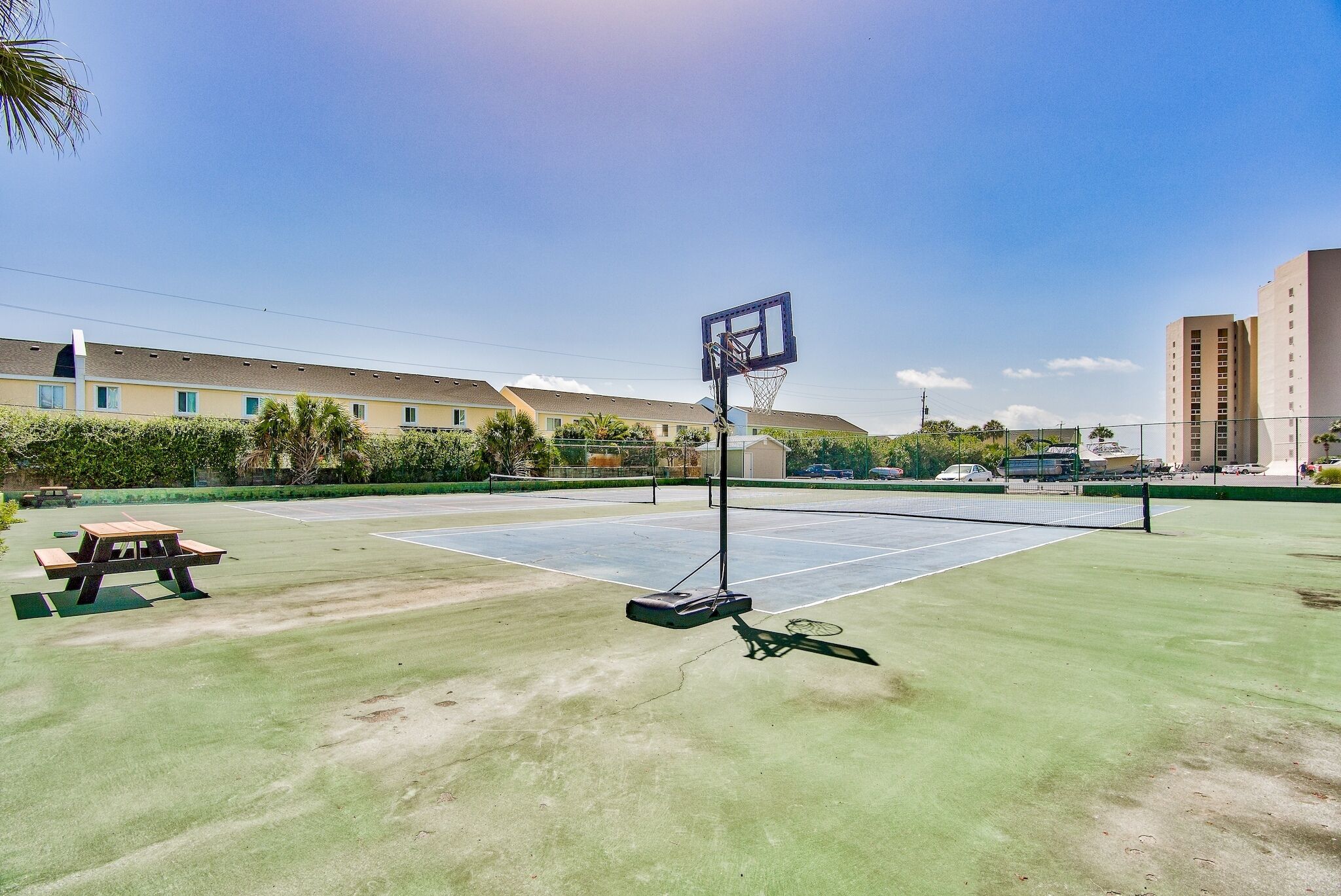 A tennis court with a net, a picnic table, and a basketball hoop.