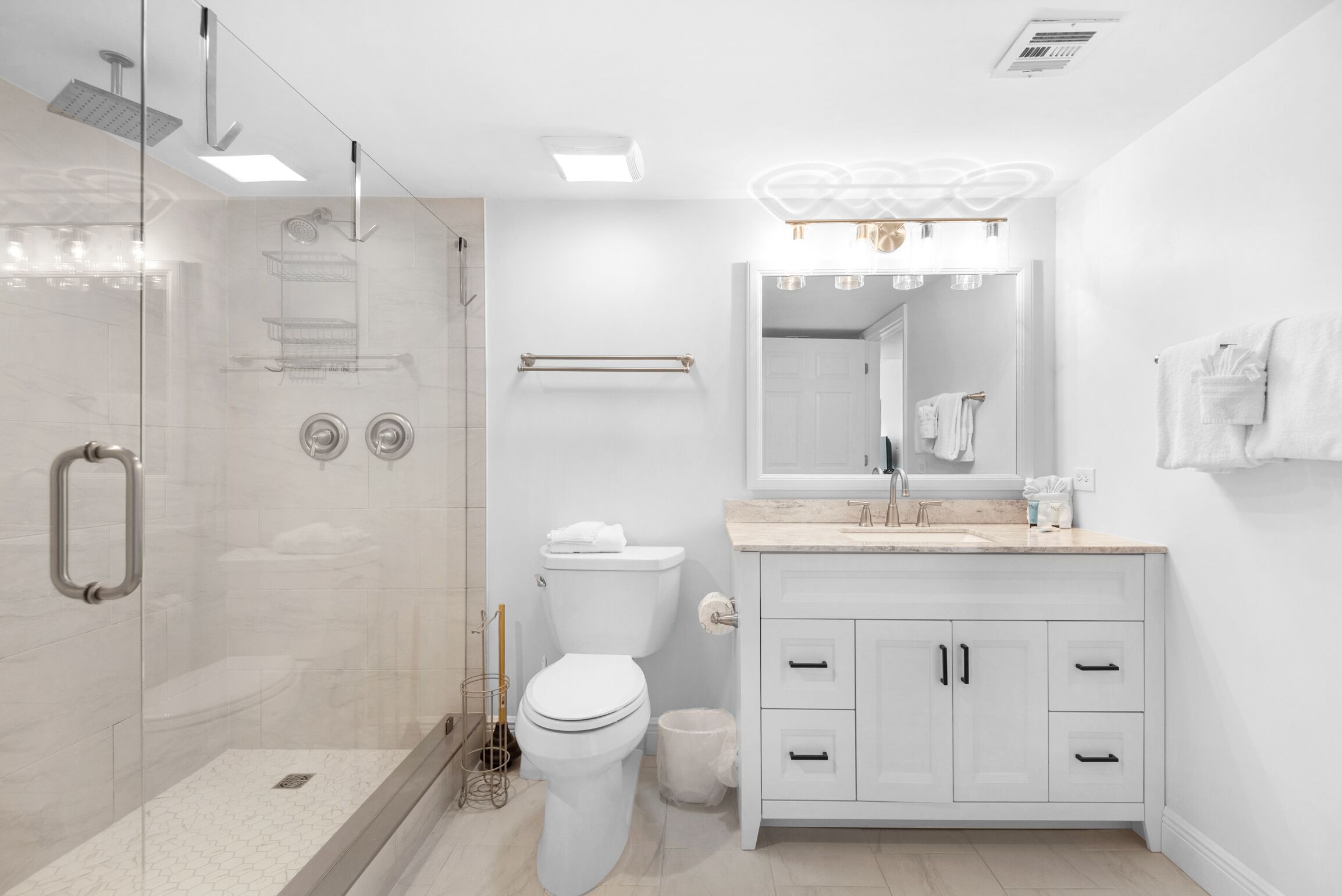 Un baño moderno con cabina de ducha de vidrio, inodoro, tocador con cajones y un espejo grande.