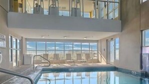 An indoor swimming pool with clear glass walls, a view of the sky, and a sunlit area with chairs and a railing. - Gulf Front! Wrap around Balcony Corner Unit, Perfect Gulf Views! CLEAN!   (Gulf Shores)