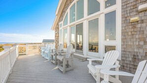 En træterrasse med hvide Adirondack-stole og et bord, med udsigt over en strand.