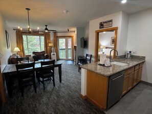 A hotel room with a dining area, kitchen, and a balcony with curtains.