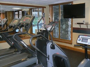Un gimnasio con cintas de correr, una bicicleta estática y un televisor montado en la pared.