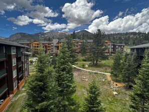 A mountain lodge with multiple-story buildings, a central courtyard with trees, and a view of snow-capped mountains.
