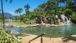 A tropical resort with a swimming pool, palm trees, and a waterfall. - Breathtaking Panoramic Bali Hai with Unobstructed Bali Hai Ocean View (Princeville)