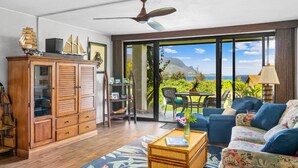 A spacious living area with a wooden cabinet, a blue sofa, a coffee table, and a ceiling fan. - Breathtaking Panoramic Bali Hai with Unobstructed Bali Hai Ocean View (Princeville)