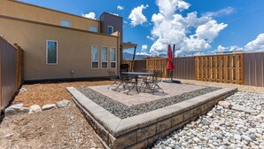 A patio with a table and chairs, a red umbrella, and a wooden fence.