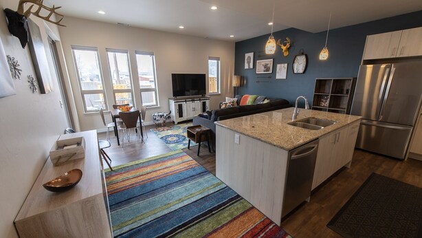 A modern kitchen with a central island, stainless steel appliances, and a colorful striped rug.