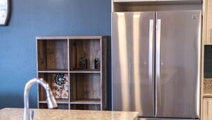 A modern kitchen with a stainless steel refrigerator, a granite countertop, and a hanging light fixture.